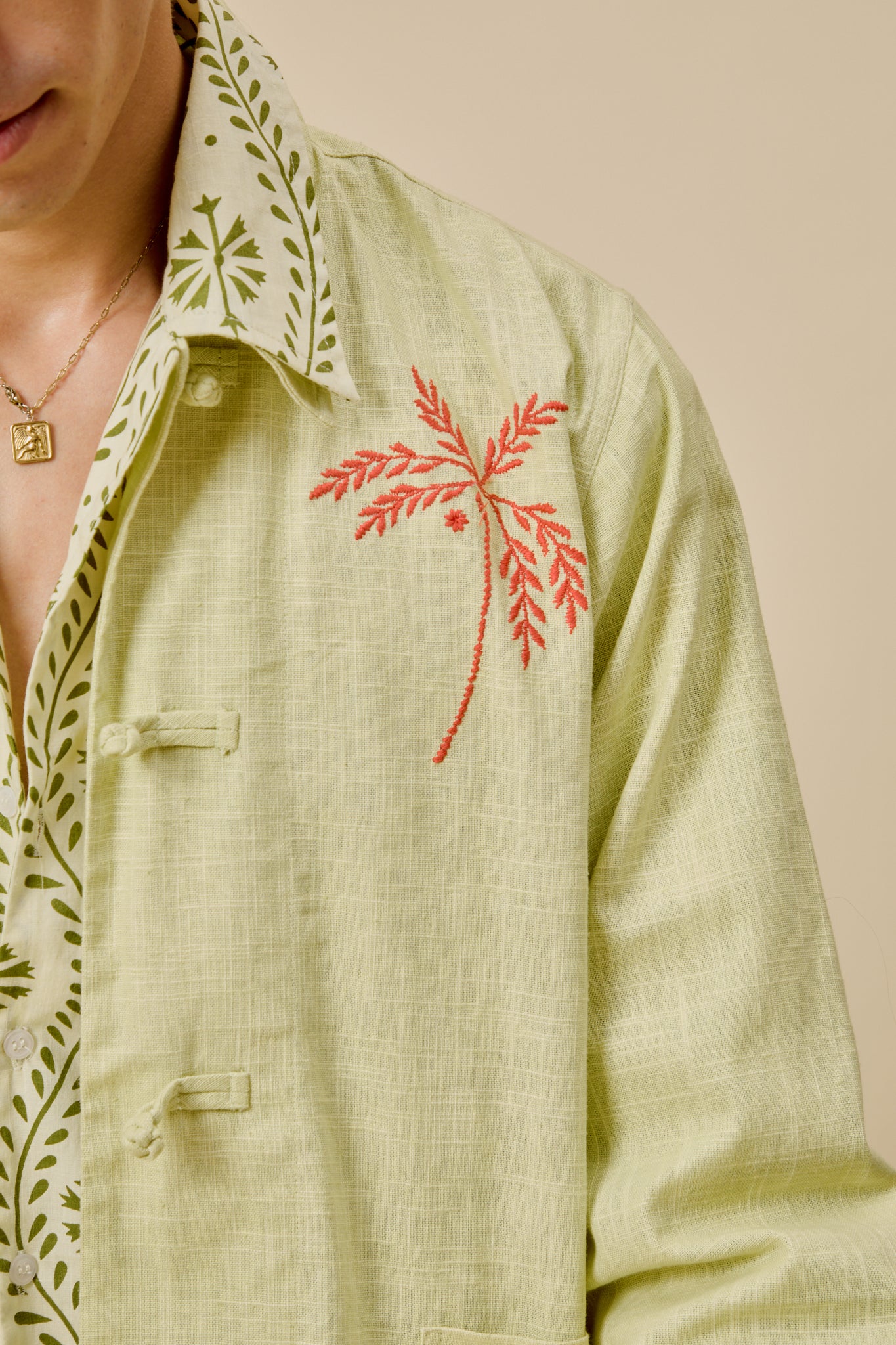 Close-up of light green jacket fabric with red palm embroidery on the front button placket.