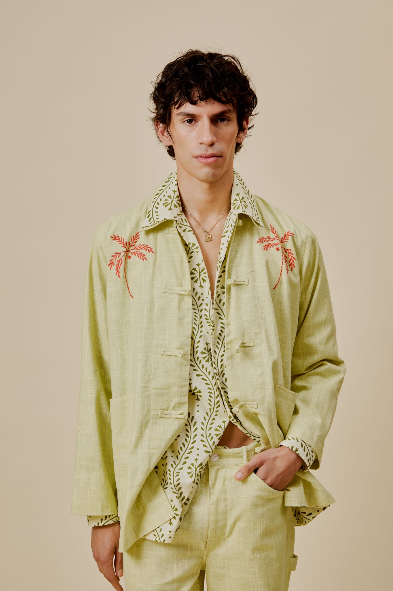Light green embroidered jacket with red palm and leafy vine accents, worn with an open collar.