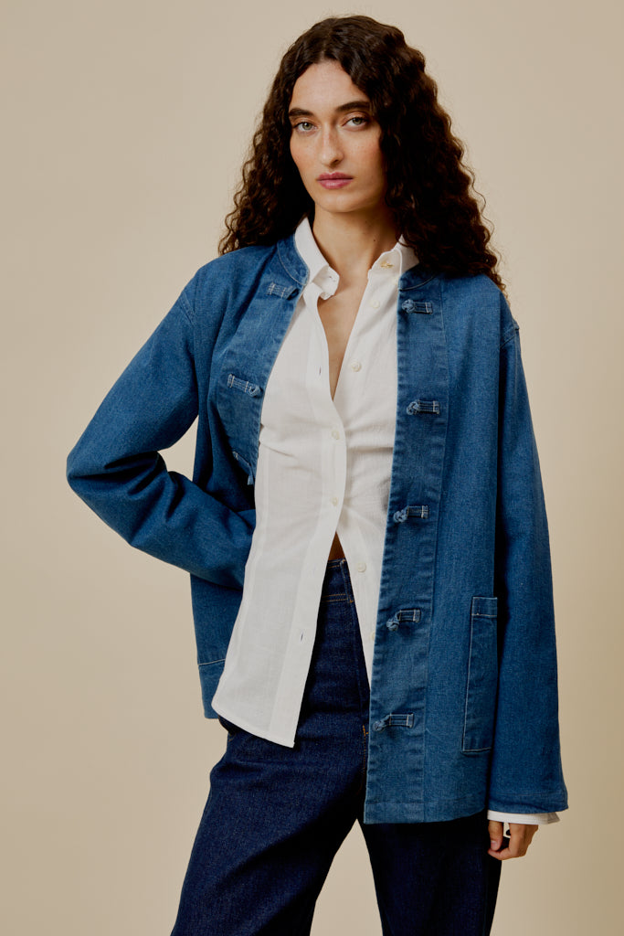 Blue denim overshirt worn open; flap chest pockets, front buttons, and long sleeves
