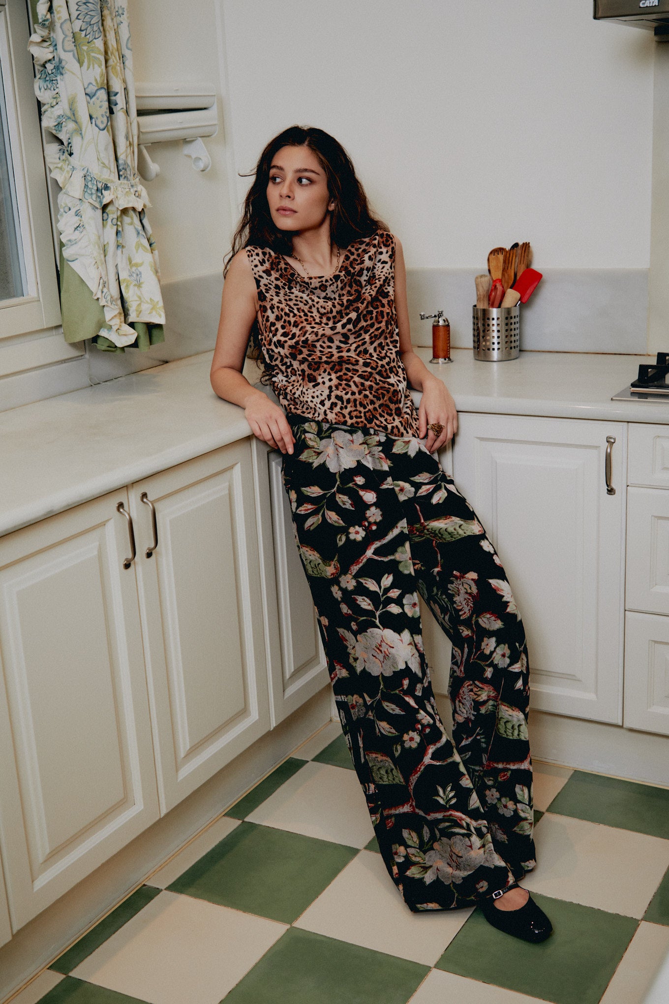 Black floral wide-leg trousers with pink and green plant print, seated pose view