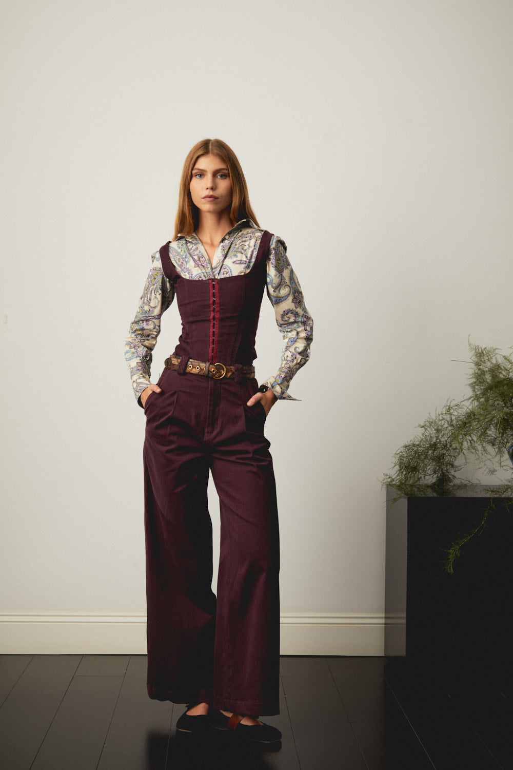 Aubergine corset with square neckline and red front lacing, worn with wide-leg trousers
