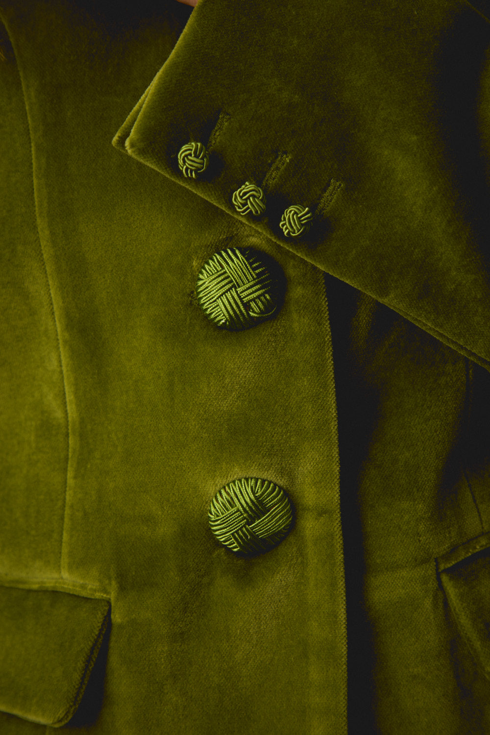 Close-up of green suede-style jacket buttons and stitched flap pocket edge