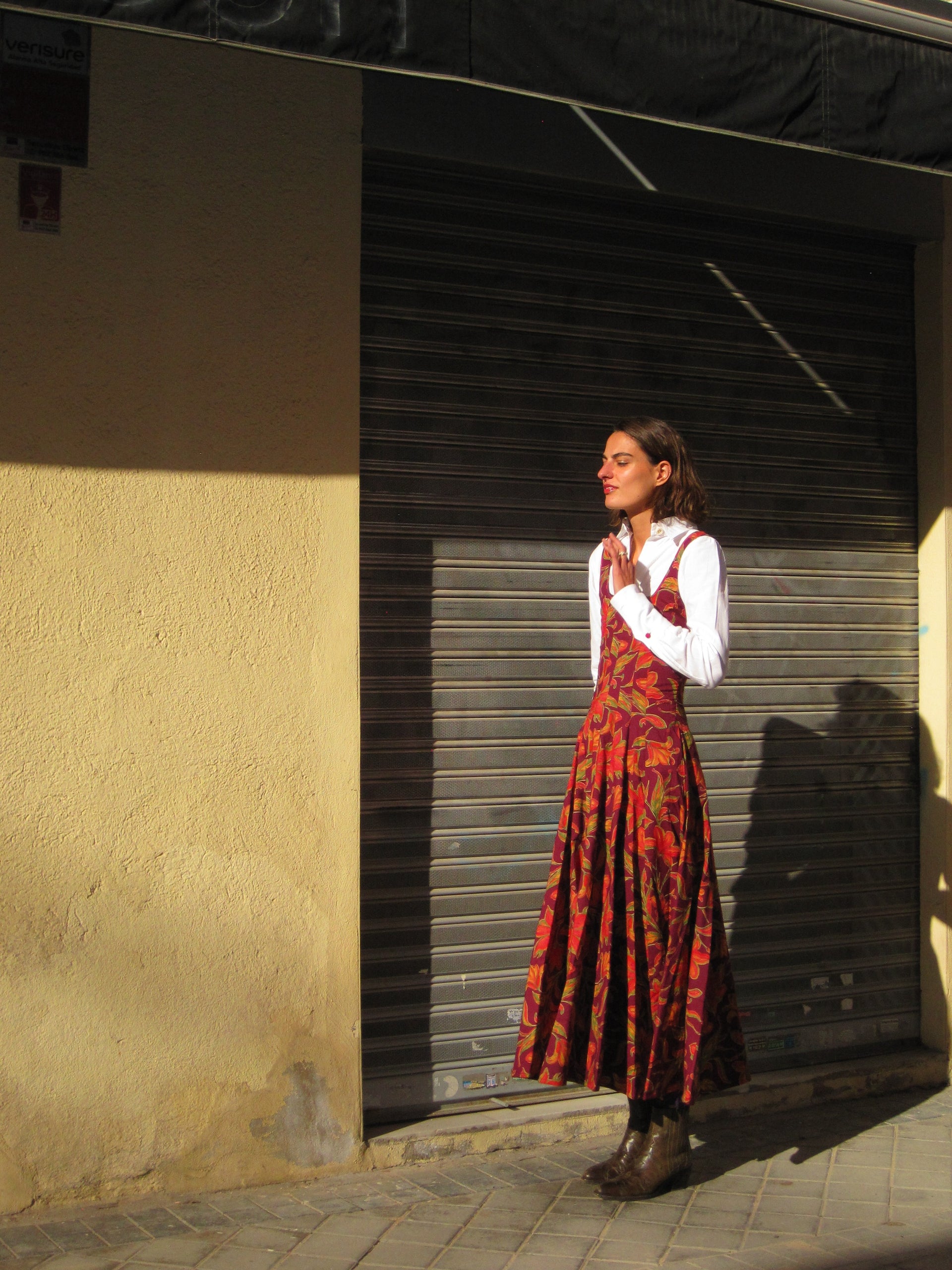 Burgundy floral pinafore-style dress over white sleeves, side view